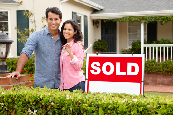 Hispanic couple outside home with sold sign